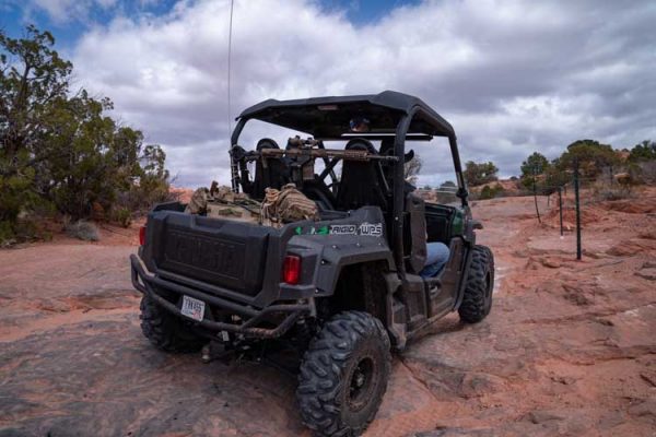 An AR-15 is mounted on a Blac-Rac 1070 with an integral lock. The Blac-Rac is mounted on a tube mount in a Yamaha Wolverine UTV. The UTV travels down an off-road path in the Utah desert.